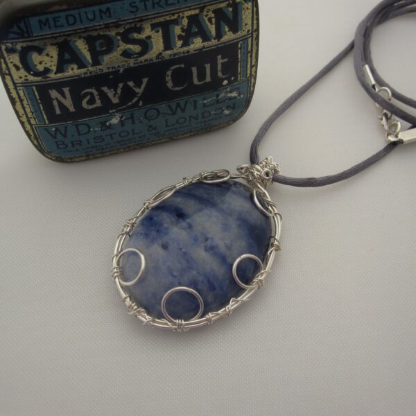 Large oval pendant featuring denim blue sodalite with a silver plated wire wrap. Hanging from grey cord 24 inches. One of a kind, designed and created in the Isle of Skye