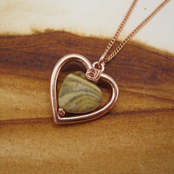 Picture of heart shaped pendant with rose gold plated frame and woodland jasper bead in centre. On rose gold plated chain.