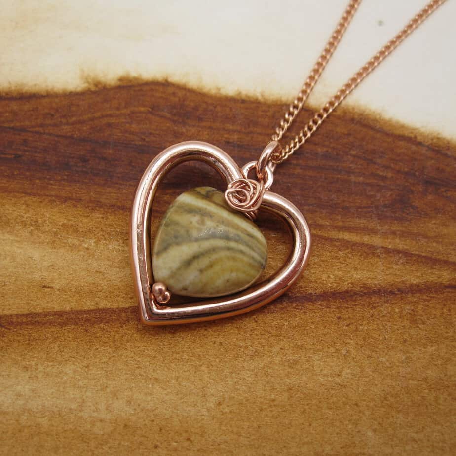 Picture of heart shaped pendant with rose gold plated frame and woodland jasper bead in centre. On rose gold plated chain.