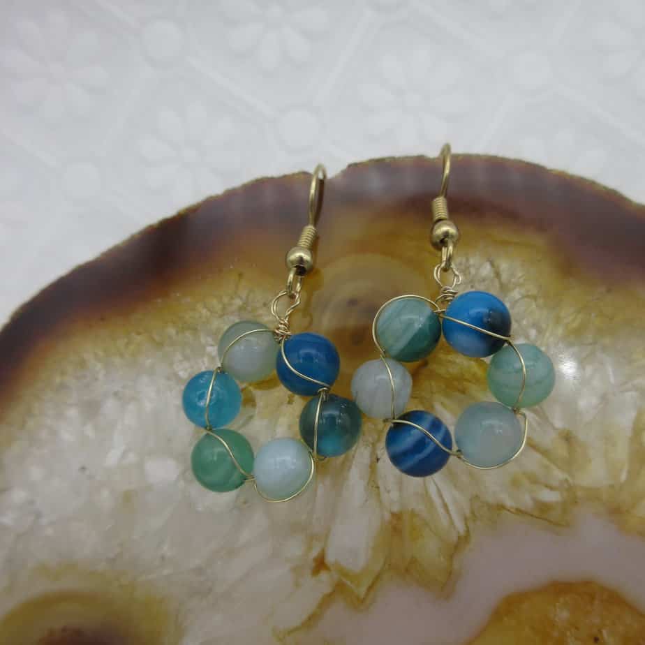 Earrings with a circle of blue and green agate round beads interwoven with gold plated wire. On gold plated shepherd hooks.