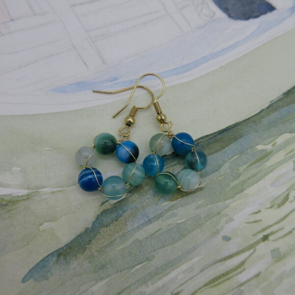 Earrings with a circle of blue and green agate round beads interwoven with gold plated wire. On gold plated shepherd hooks.