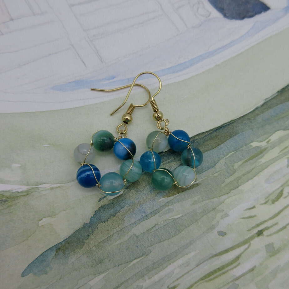 Earrings with a circle of blue and green agate round beads interwoven with gold plated wire. On gold plated shepherd hooks.