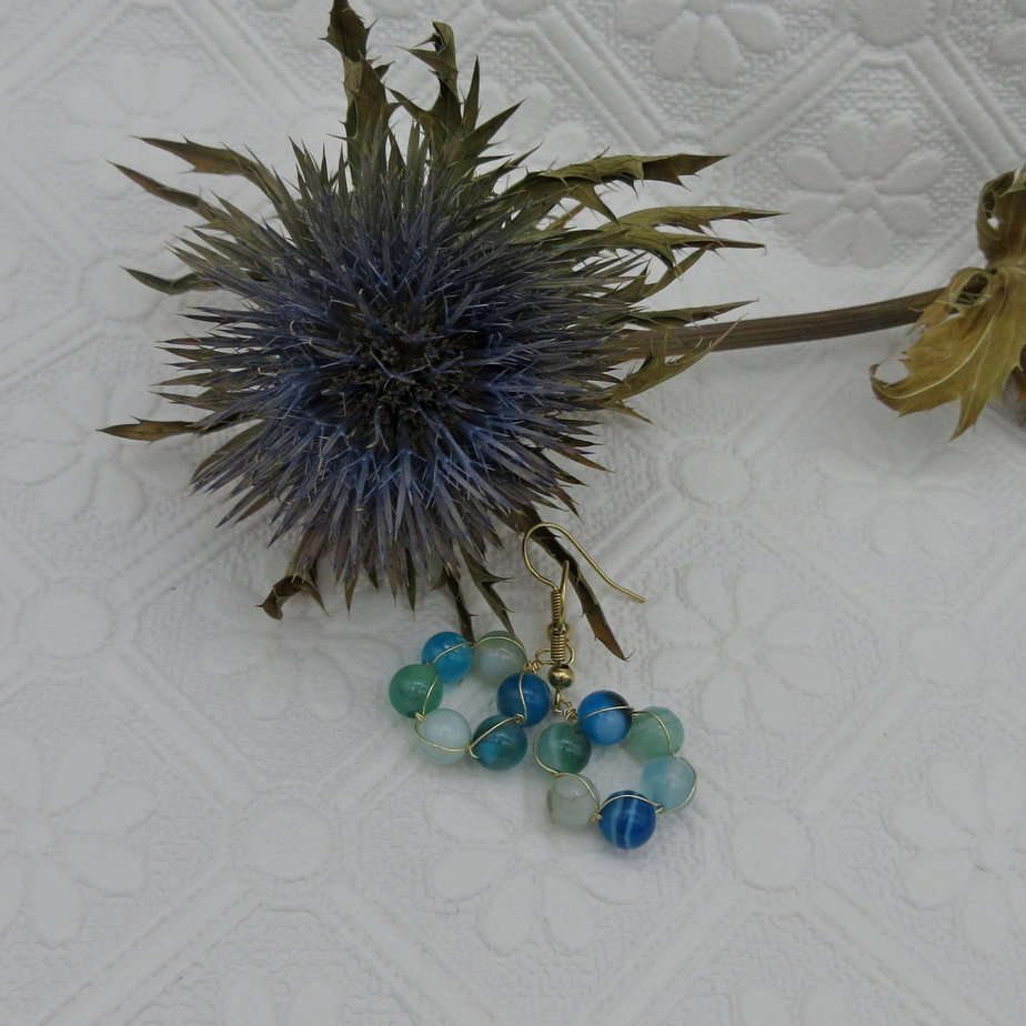 Earrings with a circle of blue and green agate round beads interwoven with gold plated wire. On gold plated shepherd hooks.