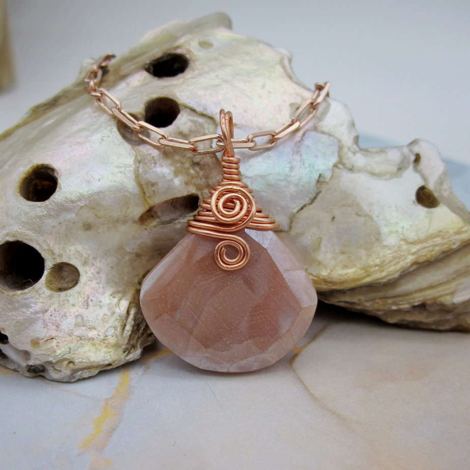 Pendant with tear drop shaped facet cut peach moonstone. With rose gold plated wire spiral and rose gold plated chain.