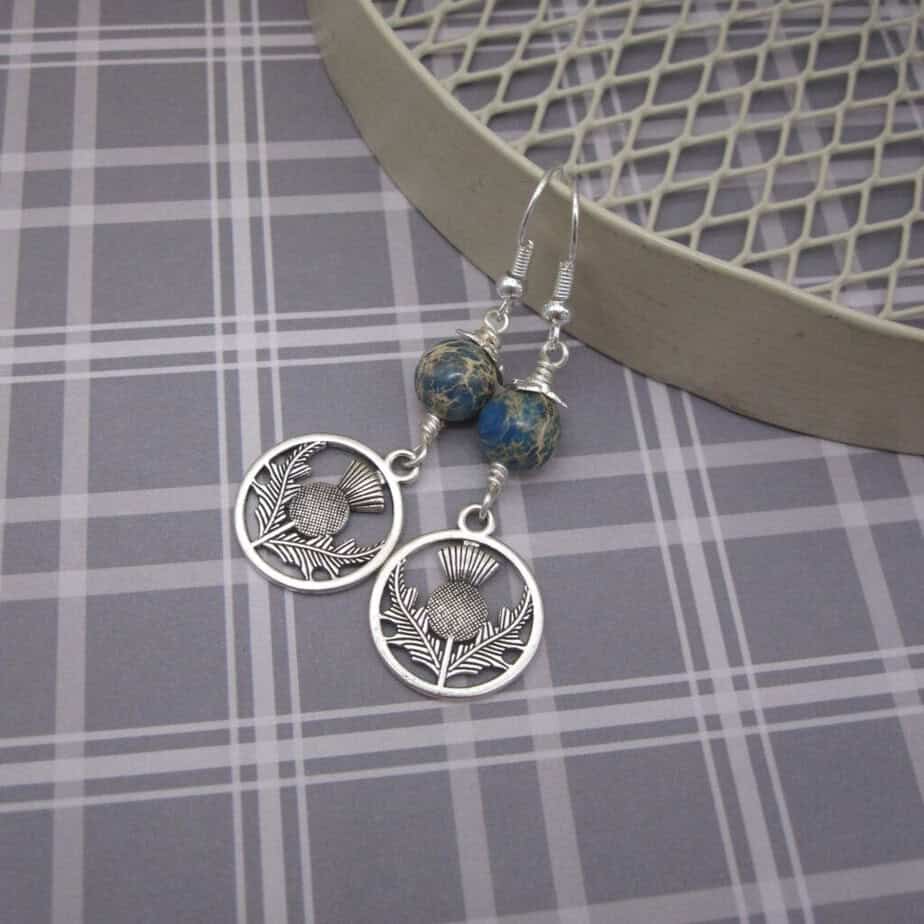 Drop earrings with round blue jasper bead and silver plated thistle charm