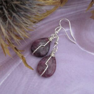 Drop earrings with tear drop shaped purple gemstone and twisted silver wire detail in flash across front.