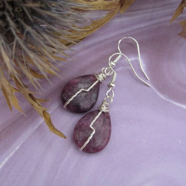 Drop earrings with tear drop shaped purple gemstone and twisted silver wire detail in flash across front.