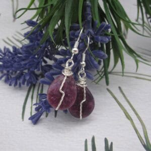 Drop earrings with tear drop shaped purple gemstone and twisted silver wire detail in flash across front.