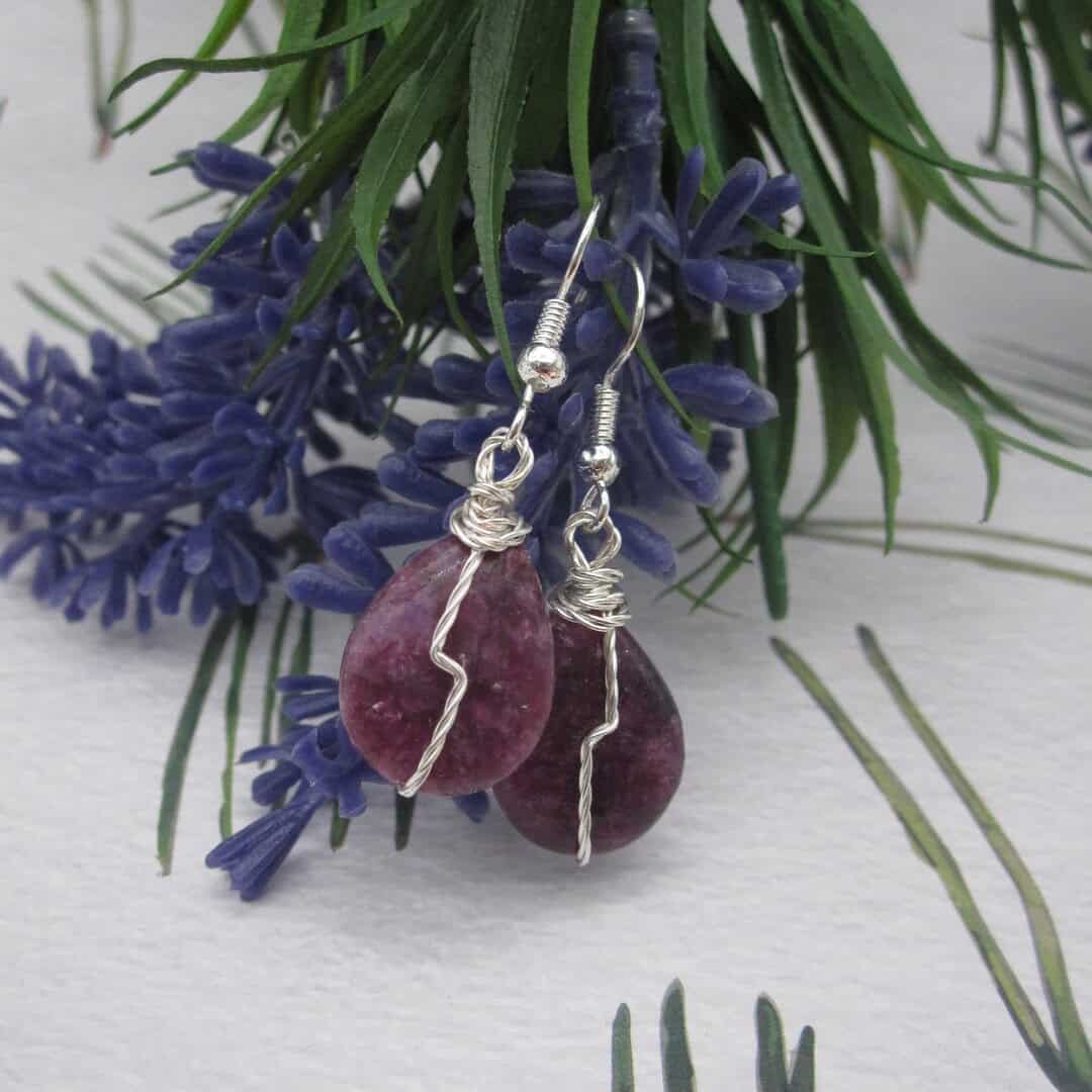 Drop earrings with tear drop shaped purple gemstone and twisted silver wire detail in flash across front.