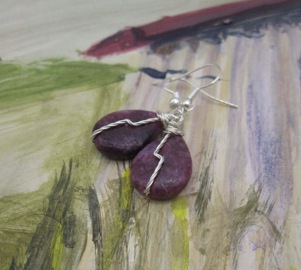 Drop earrings with tear drop shaped purple gemstone and twisted silver wire detail in flash across front.
