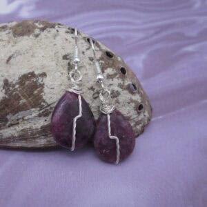 Drop earrings with tear drop shaped purple gemstone and twisted silver wire detail in flash across front.