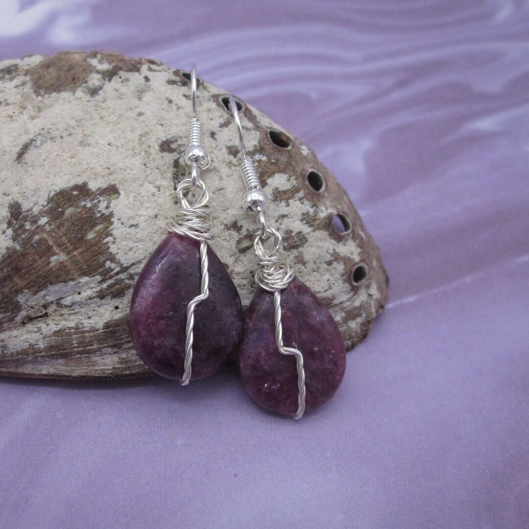 Drop earrings with tear drop shaped purple gemstone and twisted silver wire detail in flash across front.